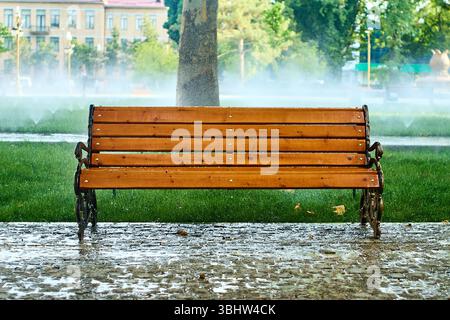 Bank und Mülltonne in einem Stadtpark von Taschkent, Usbekistan. Rasensprinkler funktionieren an einem Sommermorgen im Hintergrund Stockfoto