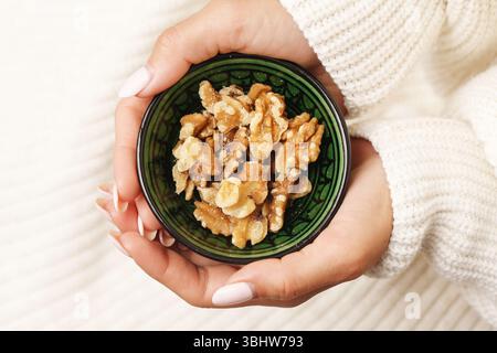 Hände halten die Schale aus Walnussholz. Gesunde Ernährung reich an Nährstoffen. Natürliche Nussmischung, Nahaufnahme der Hände. Gesunde Bio-Ernährung. Rustikales Keramikdesign. Stockfoto