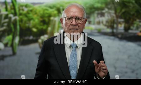 Senior Mann in einem Business-Anzug, der in einem Park mit ernsthaftem Ausdruck steht, umgeben von üppigem Grün draußen, und einen Profi und Verachtung fängt Stockfoto