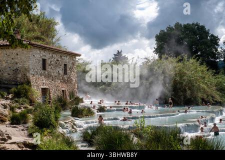 Die Menschen baden in den natürlichen sprudelnden Thermalquellen in Saturnia, Maremma, der südlichen Toskana, Italien. Das Wasser ist reich an Mineralablagerungen. Stockfoto