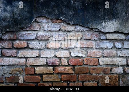 Nahaufnahme einer verwitterten orangen Ziegelwand mit rauer, gereifter Textur und Rissen. Alte Fassadentextur, die in Retro-industriellen Hintergründen und Wandoberflächen verwendet wird Stockfoto
