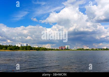 Panoramablick auf die Skyline der Stadt mit modernen Gebäuden und einem bewölkten Himmel, vom See mit ruhigem Wasser erfasst. Stockfoto