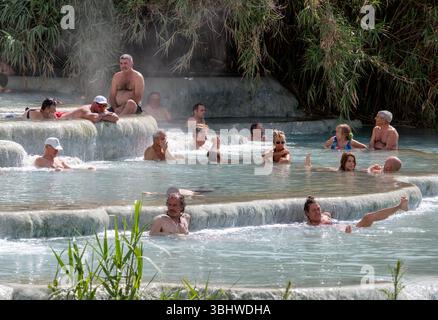 Die Menschen baden in den natürlichen sprudelnden Thermalquellen in Saturnia, Maremma, der südlichen Toskana, Italien. Das Wasser ist reich an Mineralablagerungen. Stockfoto