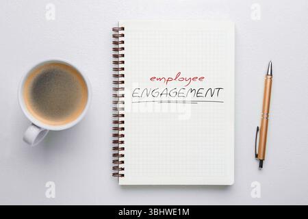 Wörter zur emotionalen Mitarbeiterbindung in Notizbuch, Stift und Kaffee auf weißem Hintergrund, Draufsicht Stockfoto