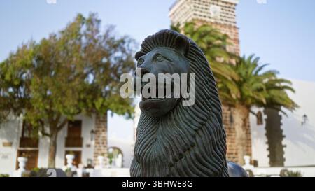 Löwenstatue im Freien teguise lanzarote kanarische Insel Tageslicht Baum Architektur Kirchturm Hintergrund Reise Stockfoto