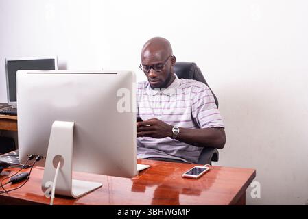 Junger seriöser Geschäftsmann, der am Schreibtisch sitzt und ein Handy benutzt. Stockfoto