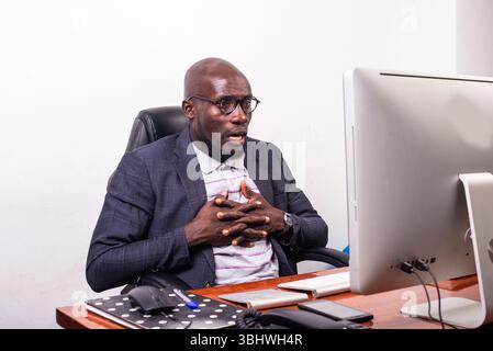 Überraschter junger Geschäftsmann mit gekreuzten Fingern auf der Brust, während er auf den Laptop-Bildschirm blickte. Stockfoto