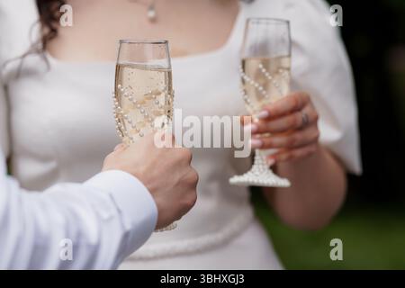 Eine fröhliche Hochzeitsszene zeigt ein Paar, das Champagner-Flöten hält, die mit Perlen verziert sind, draußen im Garten ihre vereinigung antost und romantisches Zelt überträgt Stockfoto