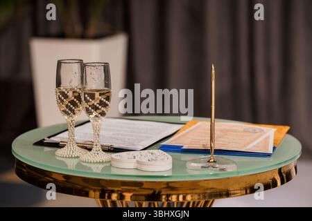 Wunderschön angeordnete Hochzeitstisch mit zwei Sektflöten, einem goldenen Stift, einem Heiratsvertrag und Hochzeitseinladungen, die einen Celebr vorschlagen Stockfoto