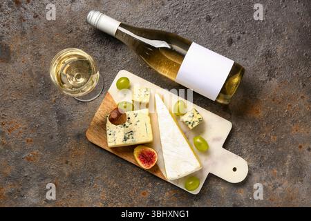 Brett mit leckerem Käse, Trauben, Flasche und Glas Wein auf braunem Hintergrund Stockfoto