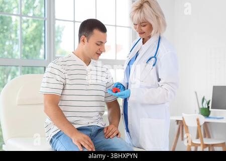 Weibliche Endokrinologin zeigt Schilddrüsenmodell beim Mann auf dem Sofa in der Klinik Stockfoto