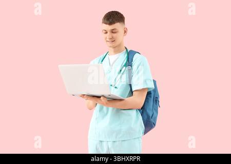 Männlicher medizinischer Praktikant mit Laptop auf rosa Hintergrund Stockfoto