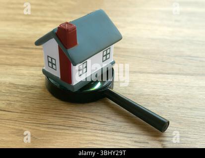 Hausmodell und Vergrößerungsglas auf Holzoberfläche - Immobilienkonzept Stockfoto