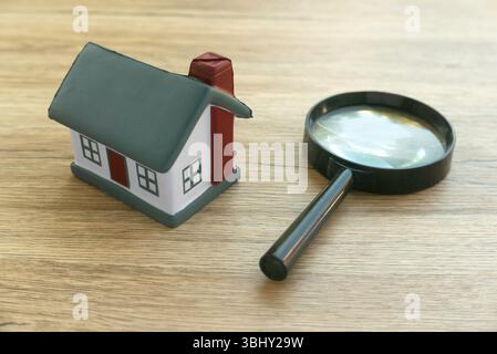 Hausmodell und Vergrößerungsglas auf Holzoberfläche - Immobilienkonzept Stockfoto