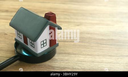 Hausmodell und Vergrößerungsglas auf Holzoberfläche - Immobilienkonzept Stockfoto