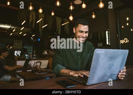 Lächelnder junger Mann, der auf einem Laptop schreibt, während er im Café arbeitet Stockfoto