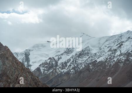 Eine majestätische Landschaft mit hoch aufragenden, schneebedeckten Bergen unter einem dramatischen, bewölkten Himmel, die die raue Schönheit der Bergkette demonstrieren Stockfoto