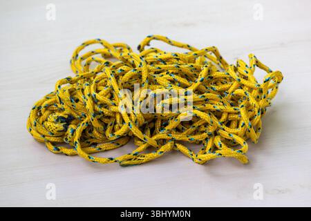 Eine Spule aus unordentlichem, aber haltbarem, farbigem Seil liegt auf einer Holzoberfläche. Dieses geflochtene Seil eignet sich zum Trocknen von Haushaltskleidung, zum Binden von Gegenständen und Stockfoto