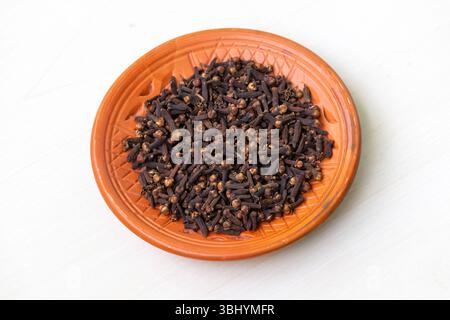 Getrocknete Nelken (Syzygium aromaticum) in Tonplatte, isoliert auf weißem Hintergrund. Stockfoto