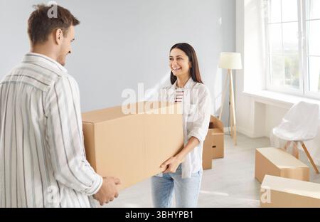 Ein glückliches, lächelndes Paar, das Pappkartons in einer neuen Wohnung trägt Stockfoto