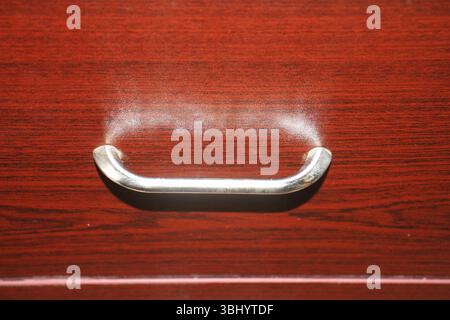 Nahansicht eines metallischen Schubladengriffs, der auf einer polierten Holzoberfläche einer Schubladenfront montiert ist. Das Holz hat einen kräftigen rötlich-braunen Farbton. Stockfoto