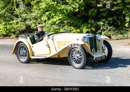 Gelbes MG-Cabriolet im Vintage-Stil auf einer sonnigen Straße mit Grün im Hintergrund und einem älteren Mann hinter dem Steuer Stockfoto