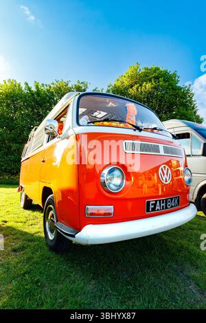 Dramatischer Weitwinkel leuchtend zweifarbig orange Vintage Typ 1 Volkswagen VW Transporter 1970er Jahre Wohnmobil auf grünem Gras unter klarem blauem Himmel geparkt Stockfoto