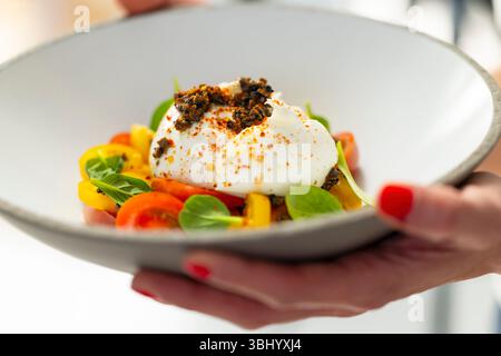 Gourmet-Burrata-Käsesalat mit Tomaten, Gewürzen und Olivenöl, gehalten von den Händen des Küchenchefs Stockfoto