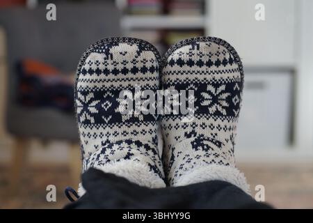 Knöchelhohe kuschelige, bequeme Hausschuhe in Blau und weiß auf einem rosafarbenen Teppich im Wohnzimmer Stockfoto
