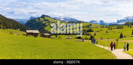 Wanderer auf einem gewundenen Pfad durch saftig grüne Wiesen mit traditionellen Holzhütten auf der Seiser Alm mit den majestätischen Dolomiten Stockfoto