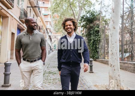 Zwei Profis genießen einen Spaziergang durch Barcelonas malerische Straßen. Bäume säumen den Weg und schaffen eine entspannte Atmosphäre, perfekt für eine Pause vom Coworki Stockfoto