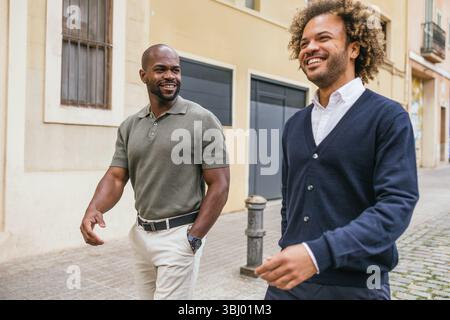 Zwei Kollegen, die in einer sonnigen Straße in Barcelona spazieren gehen und sich unterhalten, genießen ein zwangloses Meeting außerhalb des Büros. Sie wirken entspannt und engagiert Stockfoto