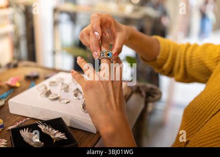 Eine Frau probiert einen detailreichen Silberring mit blauem Stein in einem Juweliergeschäft aus. In der hellen, einladenden Umgebung werden verschiedene Ringe angezeigt Stockfoto