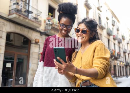 Zwei Freunde genießen einen Tag in der Stadt. Sie lächeln und tragen eine stilvolle Sonnenbrille, während sie auf ein Smartphone schauen. Die Hintergrundfunktionen Stockfoto