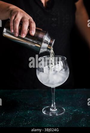 Ein Barkeeper gießt gekonnt ein erfrischendes Gin Tonic aus einem Shaker in ein mit großen Eiswürfeln gefülltes Glas, perfekt zum Kühlen und zur Aufwertung des fla Stockfoto