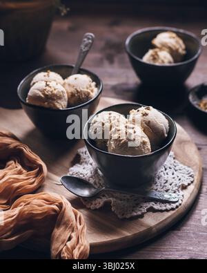 Drei Schüsseln cremiges Erdnussbutter-Eis mit griechischem Joghurt und Sahne in einem rustikalen Ambiente. Ein köstlich reichhaltiges und geschmackvolles Abendessen Stockfoto