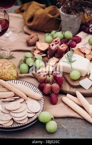 Eine rustikale Wurstplatte mit einer Auswahl an Snacks, darunter Trauben, Käse, Wurstwaren, Cracker und Brotstangen, gepaart mit einem Glas Stockfoto