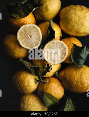 Eine lebendige Anzeige frischer, hellgelber Zitronen, ergänzt durch kontrastierende grüne Blätter. Das Bild hebt die natürliche Textur und das saftige Interieur hervor Stockfoto