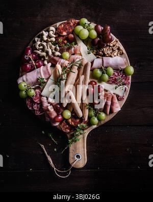 Eine schön gestaltete Wurstplatte mit einer Auswahl an Snacks, einschließlich Wurstwaren, Käse, frischen Trauben, Nüssen und Brotstangen, perfekt für Stockfoto