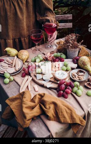 Eine rustikale Einrichtung mit einem köstlichen Käse- und Obstteller kombiniert mit zwei Gläsern Rotwein. Trauben, Birnen und eine Vielzahl von Käsesorten bilden ein pe Stockfoto