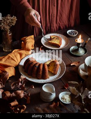 Eine gemütliche Szene mit einem hausgemachten Kürbiskuchen auf einem Holztisch. Die warme Beleuchtung unterstreicht die Konsistenz des Kuchens und die Herbstdekoration trägt zur Herbststimmung bei Stockfoto