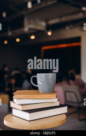 Eine ruhige Coffee-Shop-Szene mit einem Stapel Bücher und einem Becher auf einem runden Tisch. Die warme Beleuchtung und der unscharfe Hintergrund sorgen für einen gemütlichen, einladenden geldautomaten Stockfoto