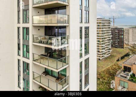 Ein zeitgenössischer Wohnkomplex mit mehreren Balkonen und eleganter Architektur vor dem Hintergrund der Stadt, der eine Mischung aus modernem Design bietet Stockfoto
