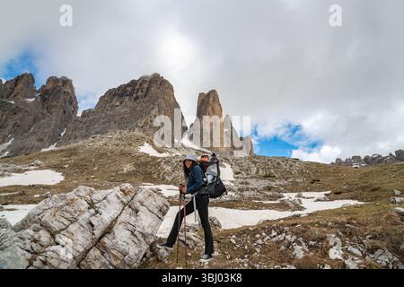Eine Mutter mit einem Baby in einer Tragetasche, die eine malerische Wanderung im majestätischen Tre Cime di Lavaredo, Dolomiten, macht. Felsiges Gelände, Schneefelder und berggebiete Stockfoto