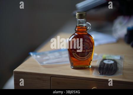 Ahornsirup in einer Glasflasche auf einem Bambuspult in der Nähe einer Packung französischer Vanilleschoten in einem dehydrierten Palstbeutel Stockfoto