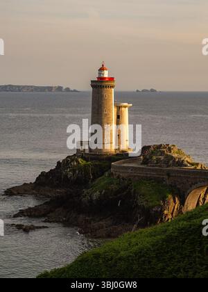 Vertikaler Blick auf den Leuchtturm Petit Minou an der Küste von Finistère, Bretagne, Frankreich, beleuchtet von goldenem Sonnenuntergang mit dramatischen Felsen und ruhigem Meer. Stockfoto