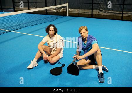 Engagierte junge Männer, die nach dem Padel-Spiel auf dem lebhaften blauen Platz scheuen. Stockfoto