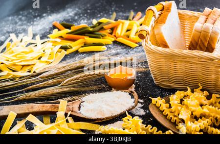 Rohe Nudeln, Brot und andere Produkte auf einem schwarzen, strukturierten Tisch Stockfoto