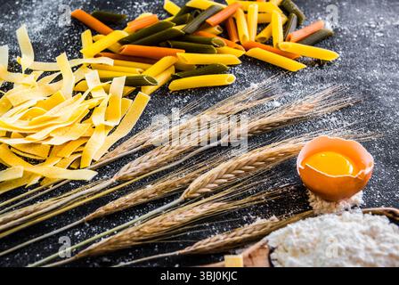 Rohe Teigwaren, Mehl und andere Produkte auf einem schwarzen, strukturierten Tisch Stockfoto