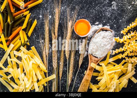 Rohe Teigwaren, Mehl und andere Produkte auf einem schwarzen, strukturierten Tisch Stockfoto